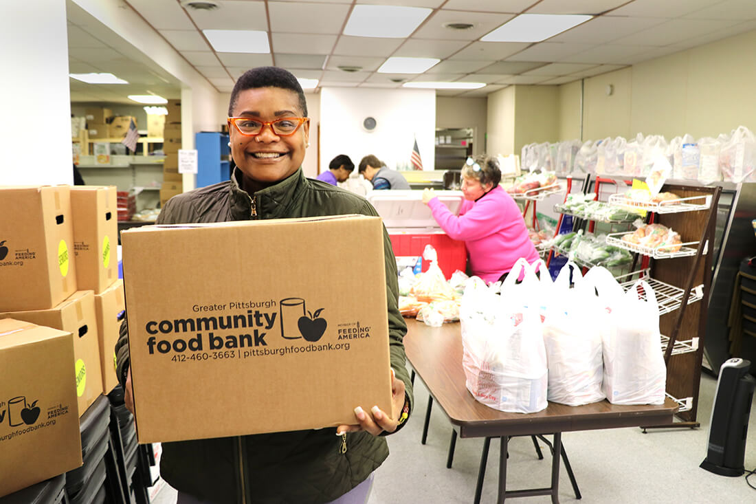 A person holding a box that has the Food Bank logo on it.